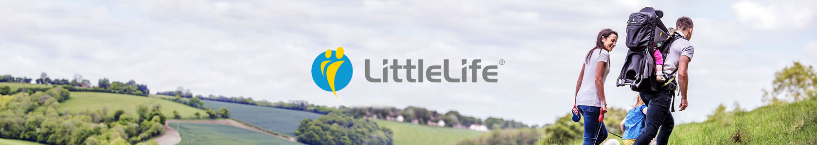 A man is carrying one child  in a LittleLife carrier on his back while another child is holding his hand and a woman is holding dog's lead, walking through fields on a cloudy day, with the littlelife logo in the center.