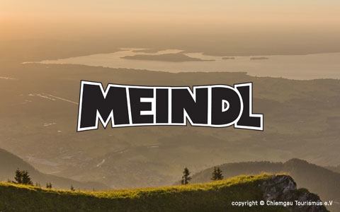 A view of land bathed in sunset light wit Meindl brand logo in the middle.