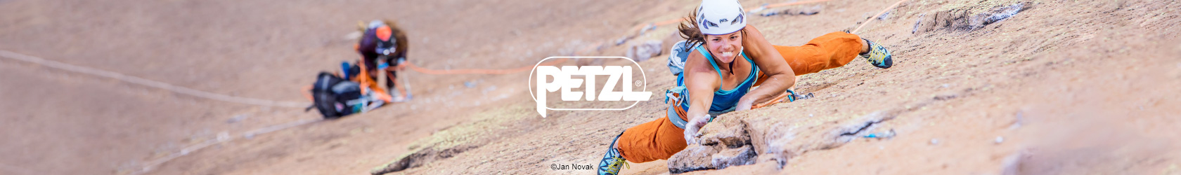 Two people are almost at the top of a rock, wearing and using Petzl gear.