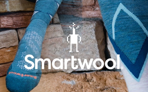 Person's feet by a stone wall, wearing Smartwool socks