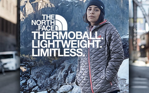 A woman, wearing a The North Face Thermoball jacket, is somewhere in the mountains with snow around and some fur trees.