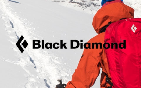 A man is walking on snow, wearing Black Diamond rucksack and trekking poles