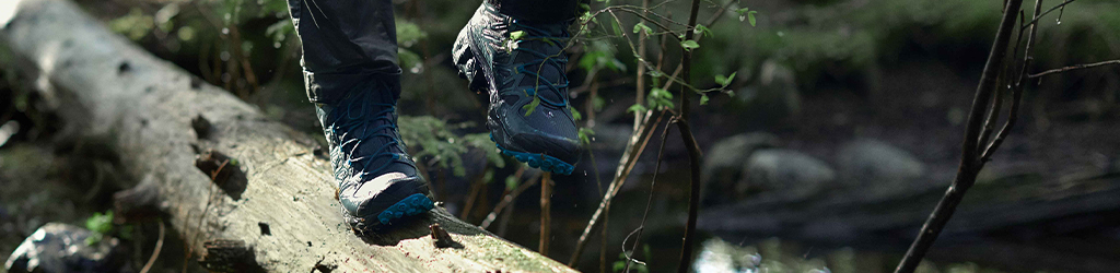 Person's feet in GORE-TEX boots, walking on a fallen tree.