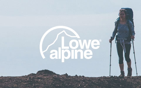 A woman stood at the top of a hill, wearing a Lowe Alpine backpack and holding walking sticks