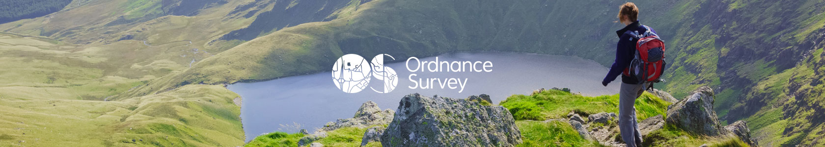 A woman is walking on a hill not far from a lake, using Ordnance Survey map