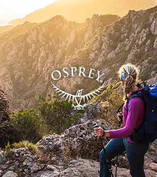 A couple with Osprey backpacks walking up a rocky hill somewhere in the mountains.