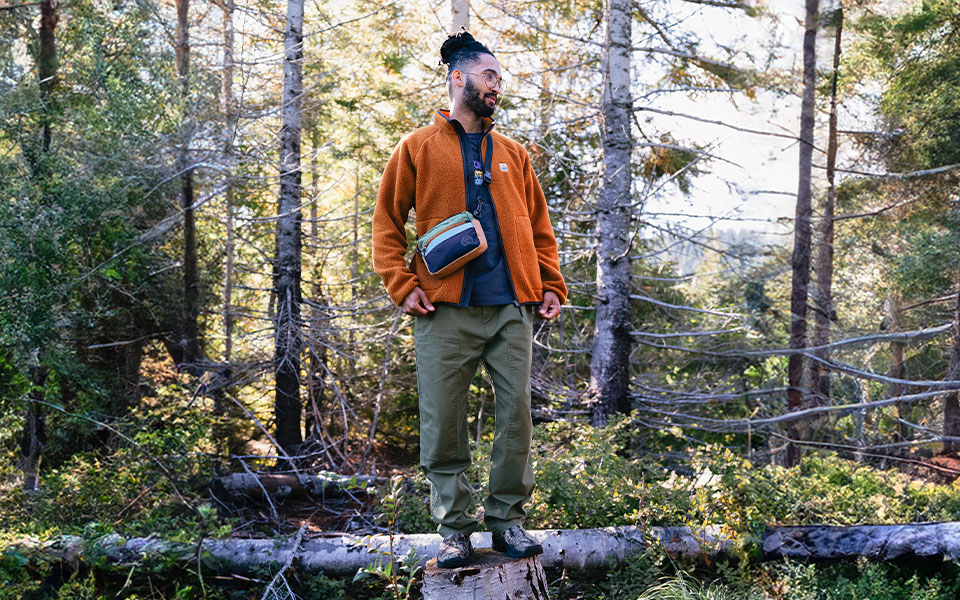 A man stood on a log in a forest wearing Passenger clothing 