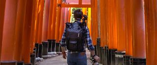 Man with hand luggage and back pack walking somewhere in Asia