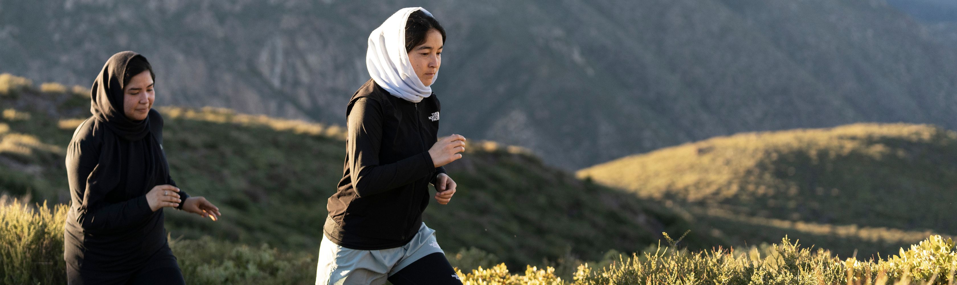 Two women wearing hijabs running through a beautiful mountain landscape