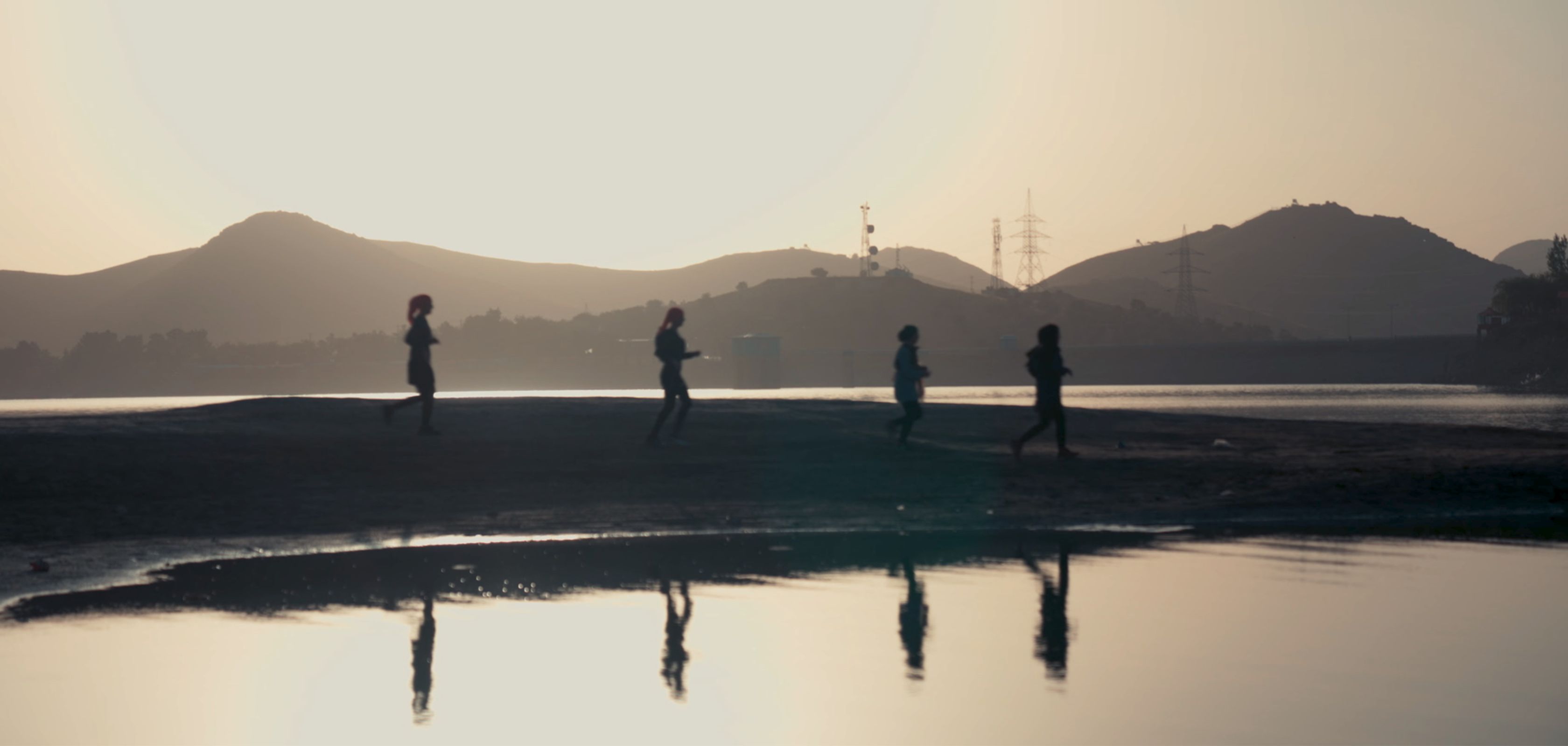 Four women running alongside a body of water 