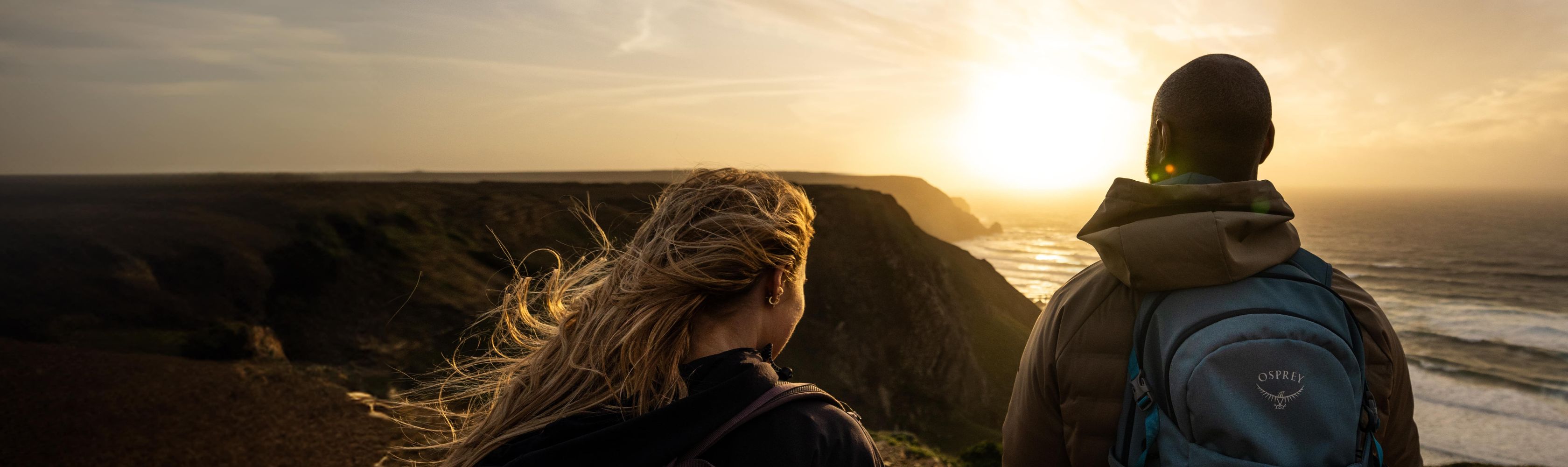 A man and a woman in the outdoors watching the sunset over the ocean