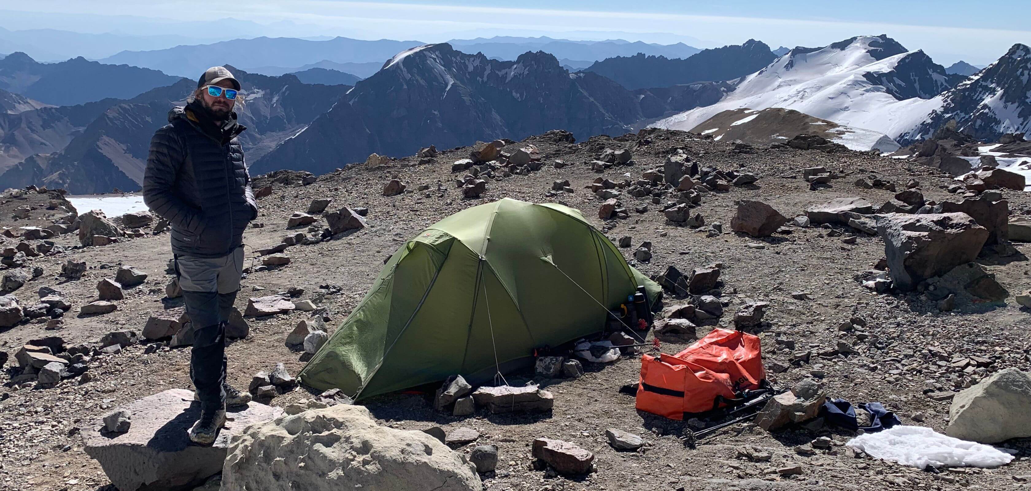 A man stood next to a tent in the mountains