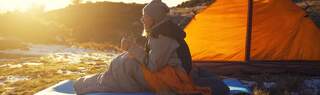 Girl sitting in a sleeping bag and drinking hot drink.