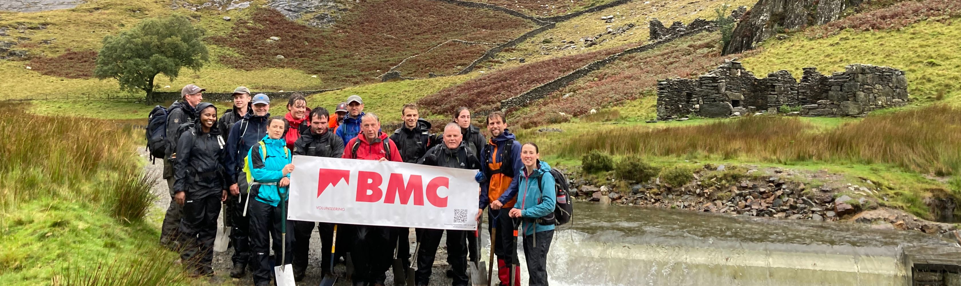 A group of people standing with a white sign that reads 'BMC' in front of a hill
