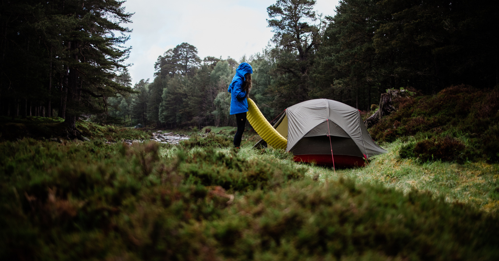 A person putting up their sleeping mat outside their tent in the middle of forest