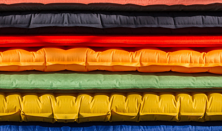 A pile of sleeping mats of varying thicknesses and designs 