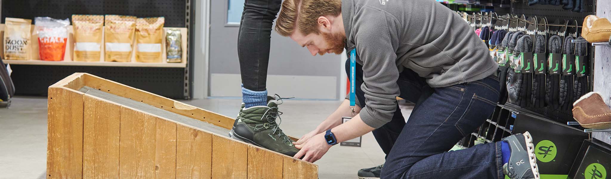 A man in a shop is fitting boots on a customer