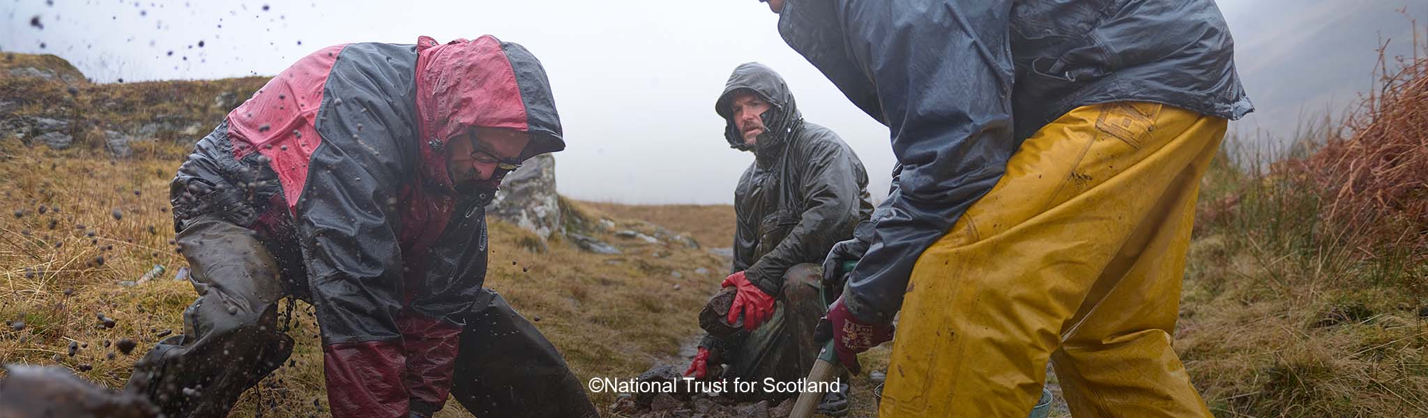 Three peope are restoring a path under the rain, wearing waterproof kit