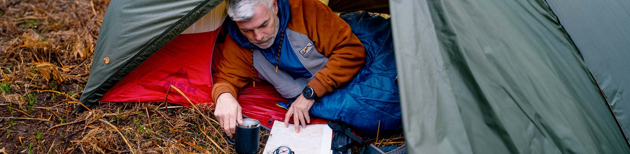 A man studying a map whilst lying on a sleeping mat 