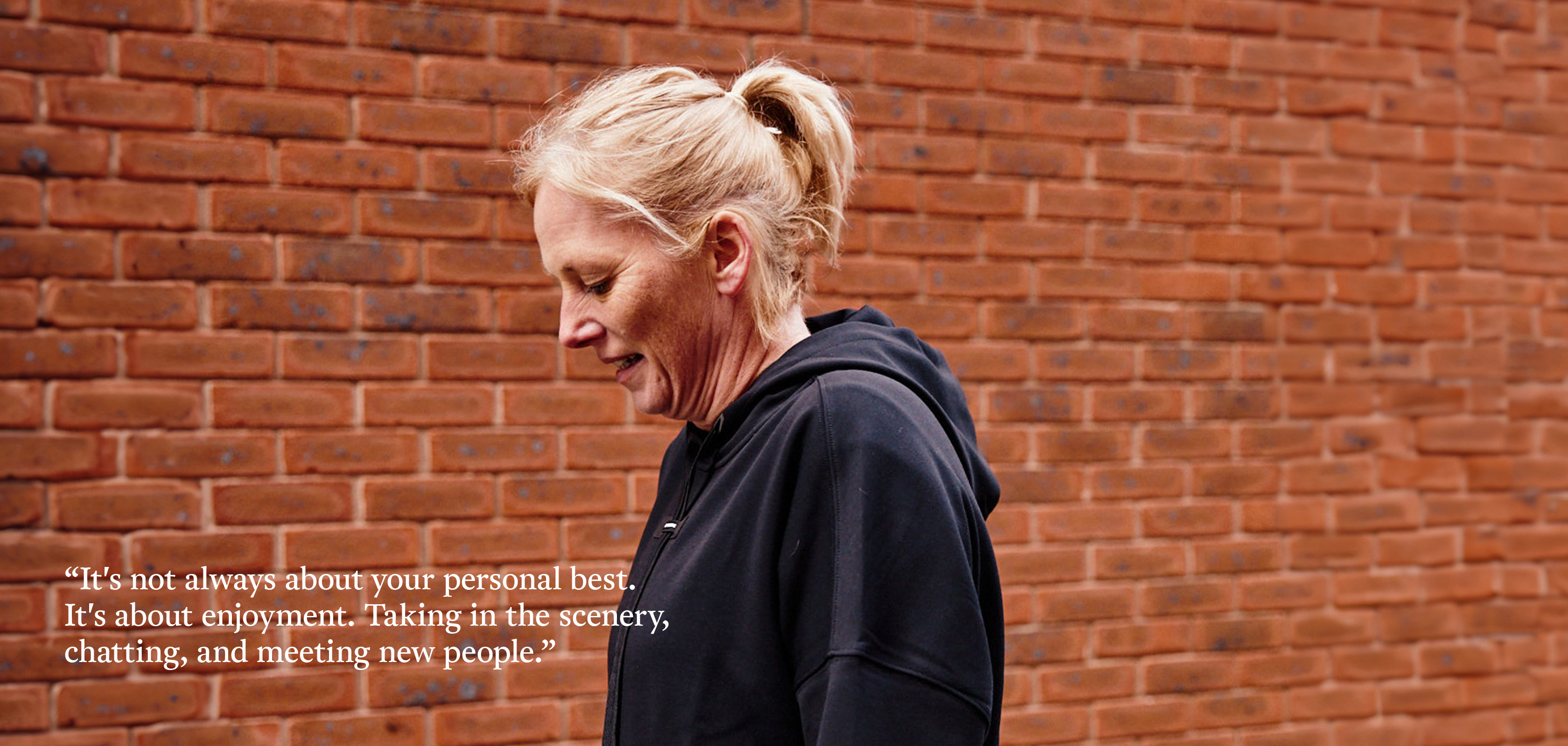 A woman with blonde hair and wearing a black hoody looking down at the ground